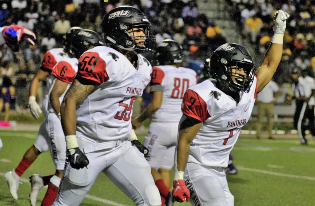 Football players in white and red trimmed uniforms walk across football field. Hands up.